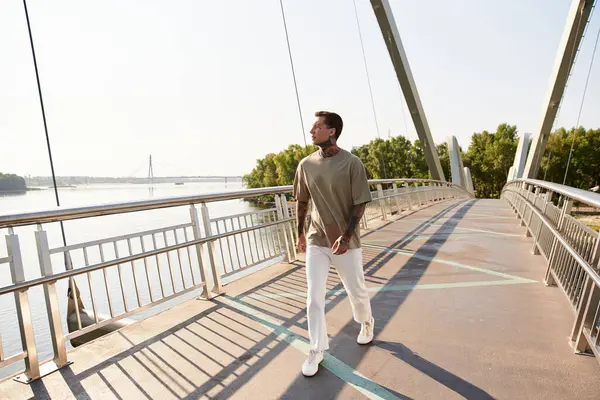 Um jovem elegante passeia em uma ponte moderna, desfrutando da luz do sol perto do rio sereno. — Fotografia de Stock