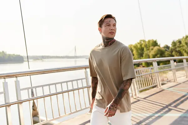 Young man with tattoos strolls along a scenic riverside path, embracing the warm sunlight. — Stock Photo