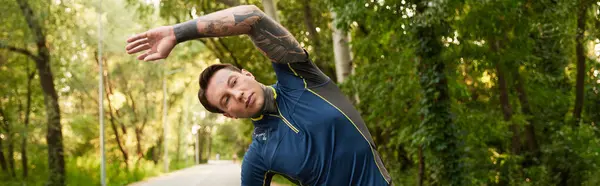 Young man stretches during a walk in a lush green park, enjoying nature and fresh air. — Stock Photo