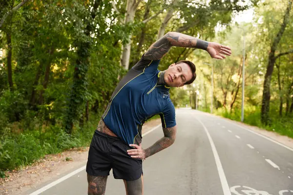 Handsome young man pauses to stretch amidst greenery on a peaceful street during his walk. — Stock Photo