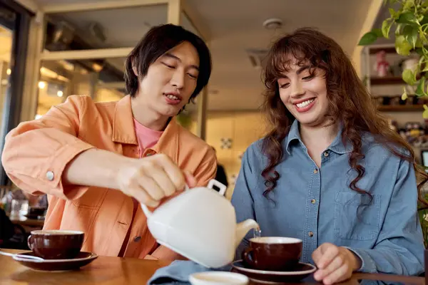 Two friends share a joyful moment while pouring tea in a vibrant cafe setting. — Stock Photo