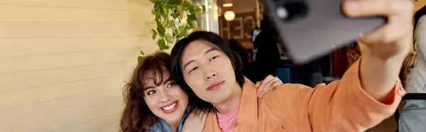 Two young multicultural friends capture a joyful selfie while sipping coffee in a lively setting, banner — Stock Photo