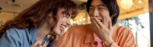 Two friends, a young Asian man and a Caucasian woman, share joyful laughter in a cozy cafe, banner — Stock Photo