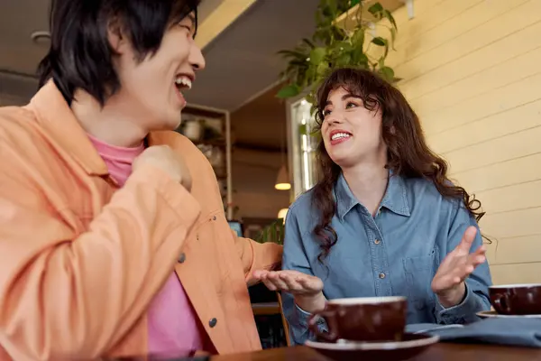 Um jovem asiático e uma mulher caucasiana desfrutar de uma conversa sincera em um ambiente de café quente. — Fotografia de Stock