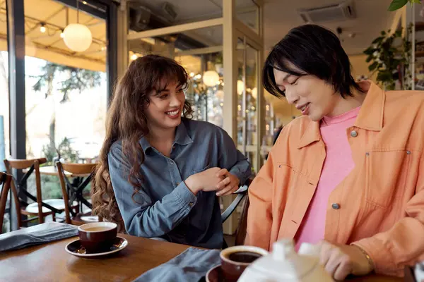 Young friends share laughter and stories in a lively cafe filled with warmth and diversity. — Stock Photo