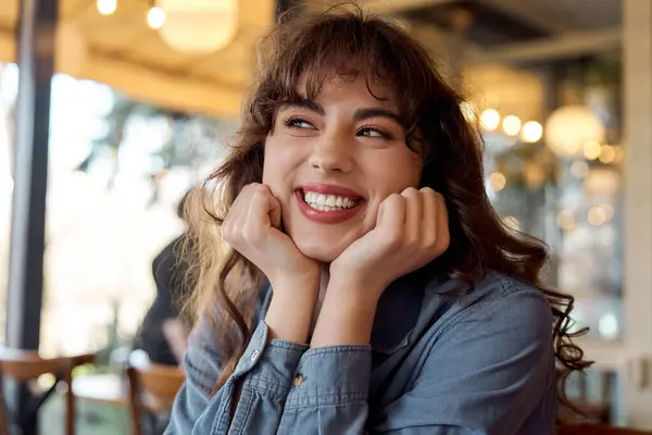 Eine junge Frau teilt Lachen und Glückseligkeit in einem lebhaften Café mit warmem Licht. — Stockfoto