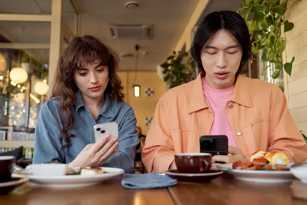 Zwei junge Freunde greifen beim Essen in einem lebhaften Café in ihre Telefone. — Stockfoto