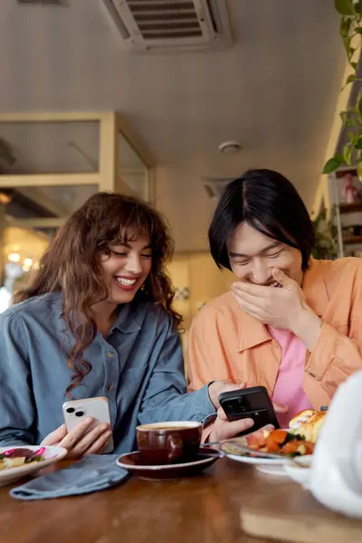 In a cozy cafe, a young asian man and woman share laughter, savoring tasty food and friendship. — Stock Photo