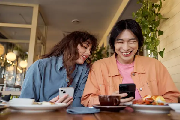 Em um café quente, os amigos compartilham risos enquanto verificam seus telefones e desfrutam do brunch juntos. — Fotografia de Stock