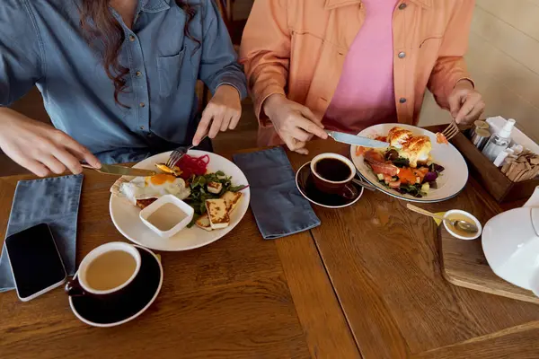 Two friends savor delicious brunch dishes and coffee while sharing joyful moments. — Stock Photo