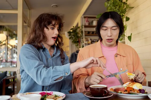 Due amici multiculturali si godono il brunch insieme, condividendo risate e cibo delizioso in un caffè. — Foto stock