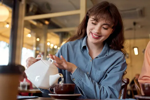 Happy young woman pouring tea in a cafe — Stock Photo