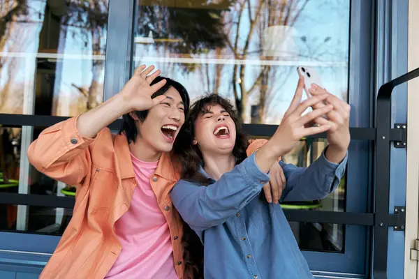 Two young friends, a man and a woman, share laughter while taking a selfie in a vibrant cafe. — Stock Photo