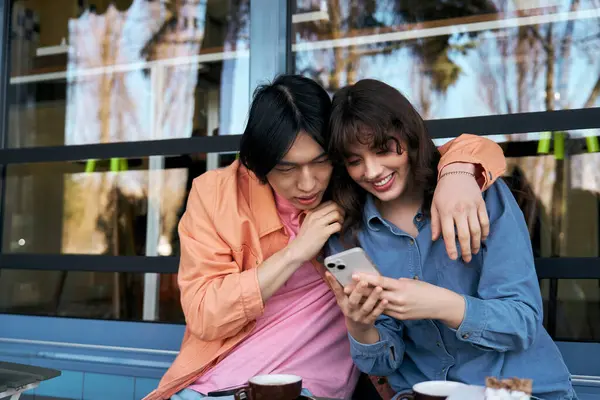 A young Asian man and woman share a joyful moment while browsing a phone together in a cozy cafe. — Stock Photo