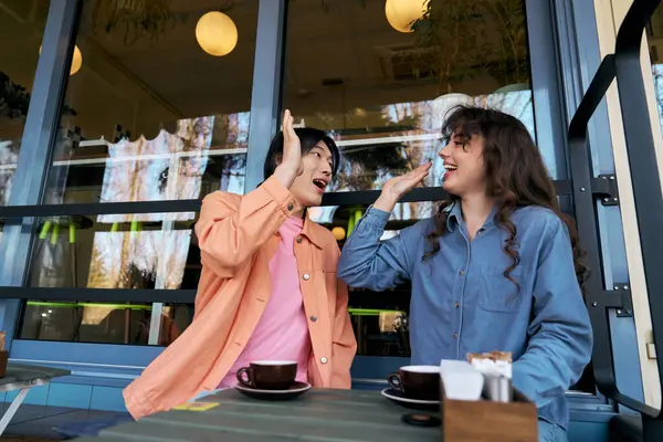 Deux jeunes amis rient ensemble dans un café, partageant un moment lumineux rempli de joie. — Photo de stock