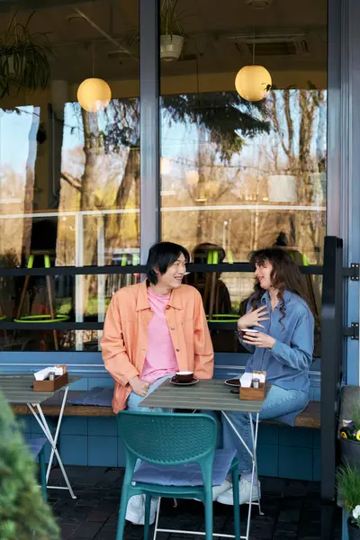 Two young friends enjoy a lively conversation in a vibrant cafe filled with natural light. — Stock Photo