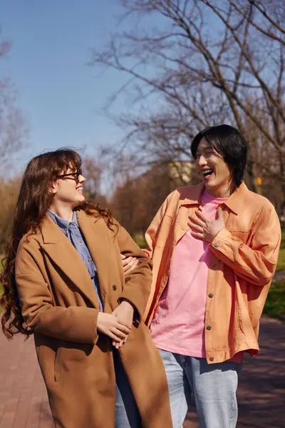 Two young friends, an Asian man and a Caucasian woman, enjoy a sunny day strolling in the park. — Stock Photo