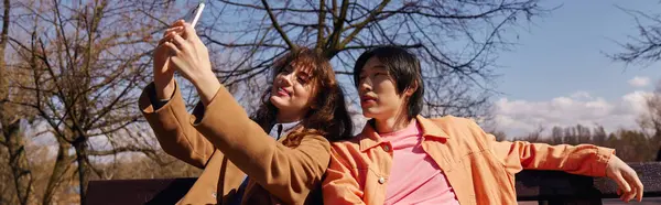 Dos jóvenes amigos, un hombre y una mujer, se toman una selfie en el parque bajo cielos despejados, pancarta - foto de stock