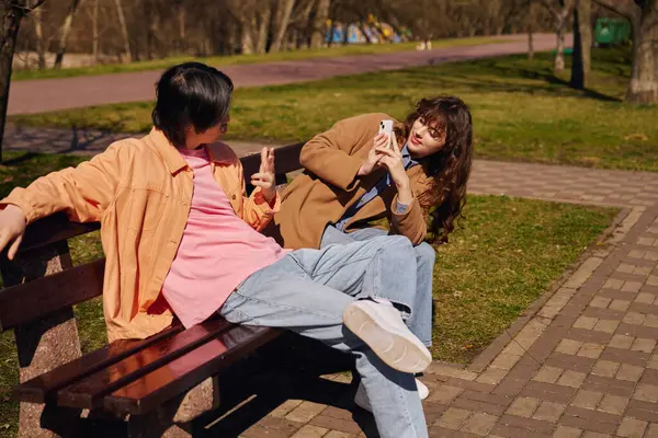 Two young friends relax on a bench, enjoying a lovely day in the park as they connect and laugh. — Stock Photo