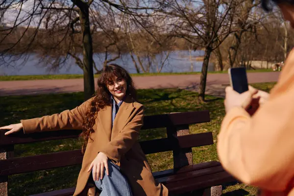 Two friends in the park, person is taking photo of a friend on a bench — Stock Photo