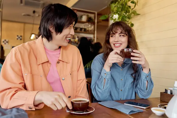 Em um animado café, um jovem asiático e uma mulher multicultural compartilham café e sorrisos.. — Fotografia de Stock