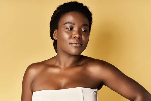 Jeune femme afro-américaine présente sa belle peau sur un fond jaune chaud. — Photo de stock