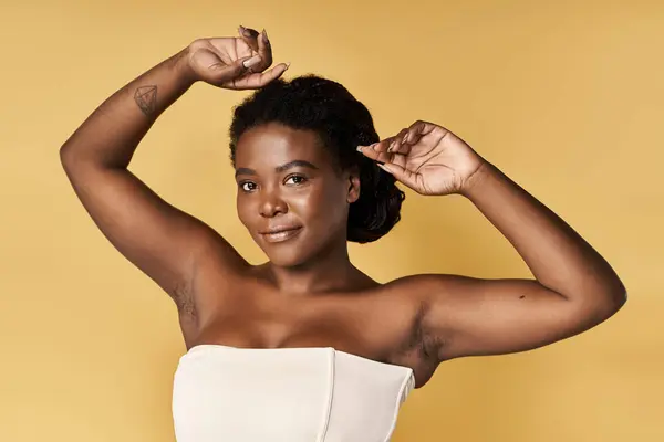 Young woman showcases radiant skin and raising hands, showing armpits, against a yellow backdrop in a studio. — Stock Photo