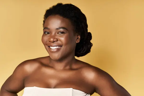 A young African American woman smiles confidently against a warm studio backdrop. — Stock Photo