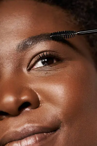 Young woman with radiant skin applies mascara, showcasing confidence and beauty in a studio. — Stock Photo
