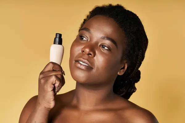 A young African American woman holds a beauty product, showcasing her healthy, glowing skin. — Stock Photo