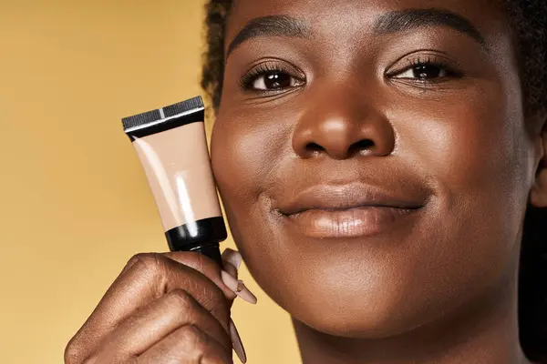 Uma jovem afro-americana exibe sua pele impecável enquanto segura um produto de beleza. — Fotografia de Stock