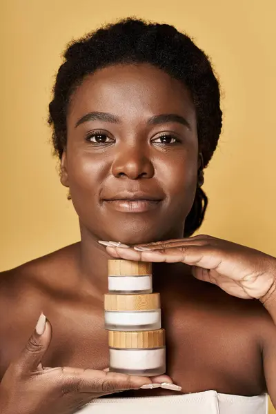 A young African American woman shows off her radiant skin with skincare products in a studio. — Stock Photo