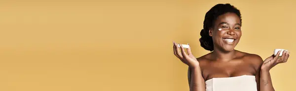 A young Black woman displays her radiant skin and smiles while holding skincare products, banner — Stock Photo