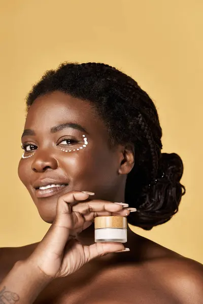Bright-backgrounded young woman with glowing skin smiles while showing her skincare product. — Stock Photo