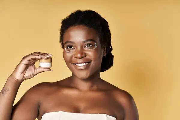 A young African American woman showcases her beautiful skin while holding a skin care product. — Stock Photo