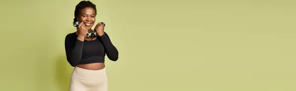 Mujer afroamericana joven sonríe mientras se prepara para un entrenamiento atractivo en un estudio vibrante, pancarta - foto de stock