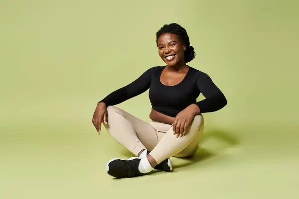 Jovem esportista afro-americana sorri enquanto se senta no chão do estúdio depois de se exercitar. — Fotografia de Stock