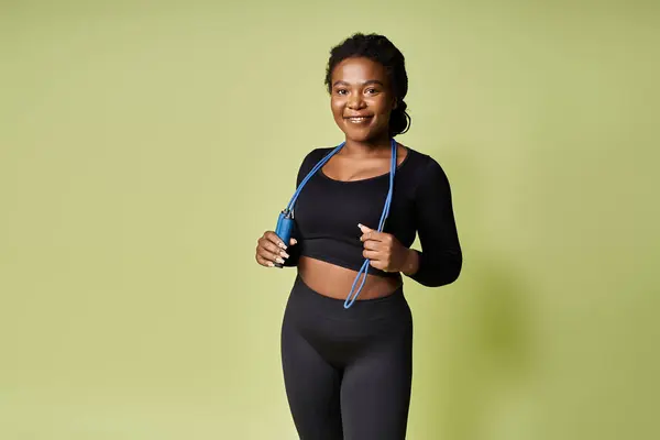Confident sportswoman holds a jump rope, ready to begin her workout in a vibrant studio setting. — Stock Photo