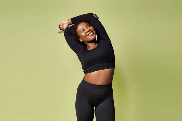 Uma jovem mulher americana africana confiante alonga alegremente seu corpo enquanto exercita. — Fotografia de Stock