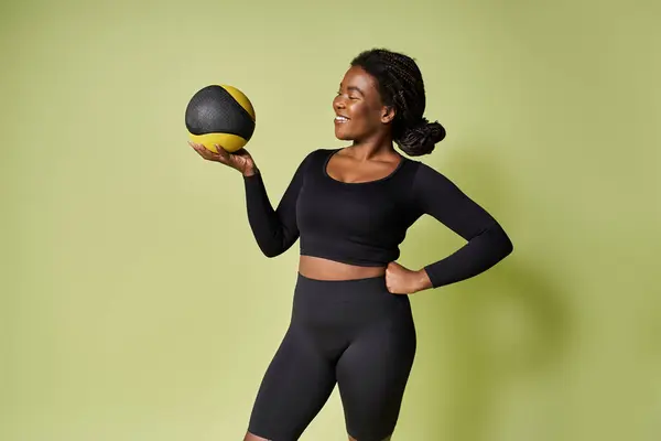 A young, fit African American athlete smiles while balancing a workout ball. — Stock Photo