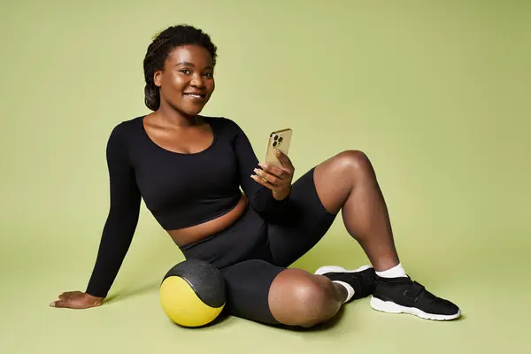 Una joven deportista se relaja con su teléfono después de una sesión de entrenamiento energizante en un vibrante estudio. - foto de stock