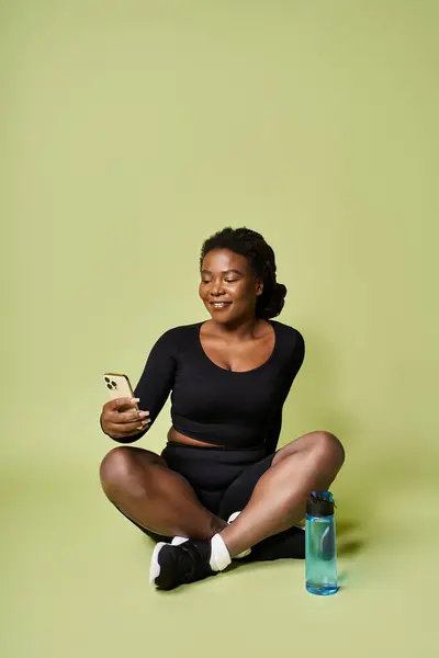 Ajuste mujer afroamericana disfruta del entrenamiento mientras revisa su teléfono en un vibrante espacio de estudio. - foto de stock
