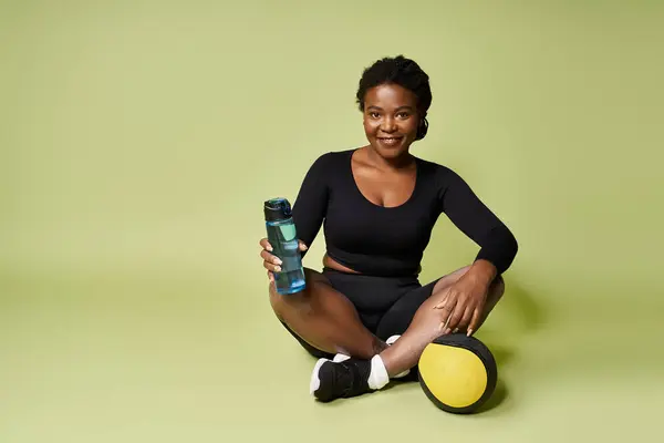 Athletic young woman enjoying her workout while sitting on the floor with equipment in a studio. — Stock Photo