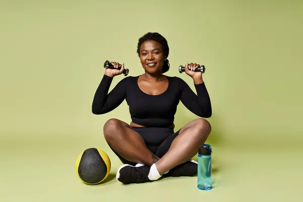A young African American woman exercises with weights while sitting comfortably on the floor. — Stock Photo