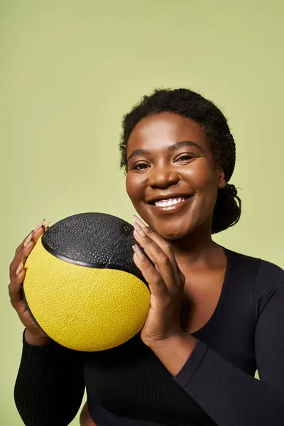 Young African American woman enjoys a workout session while holding a medicine ball in a studio. — Stock Photo