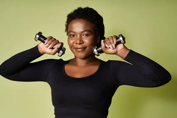 Confident African American woman workouts with dumbbells in a vibrant studio, radiating motivation. — Stock Photo