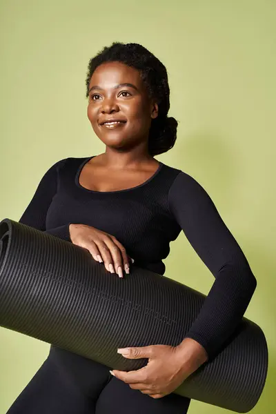 Young African American woman holds exercise mat, ready for a motivating workout session. — Stock Photo