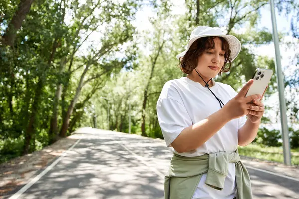 A young woman enjoys a sunny summer day while checking her phone outdoors among lush trees. — Stock Photo
