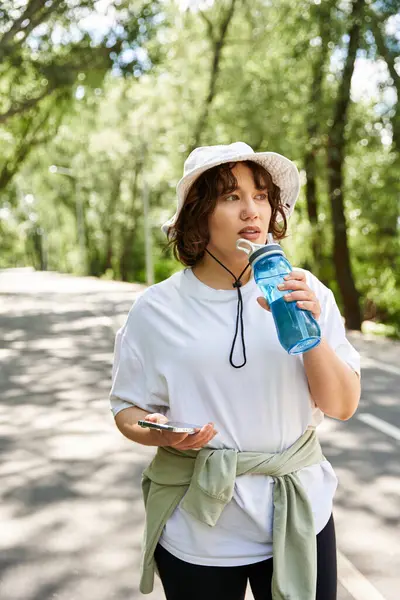 Une jeune femme arrête sa routine d'exercice à l'extérieur, sirotant de l'eau tout en restant hydratée. — Photo de stock