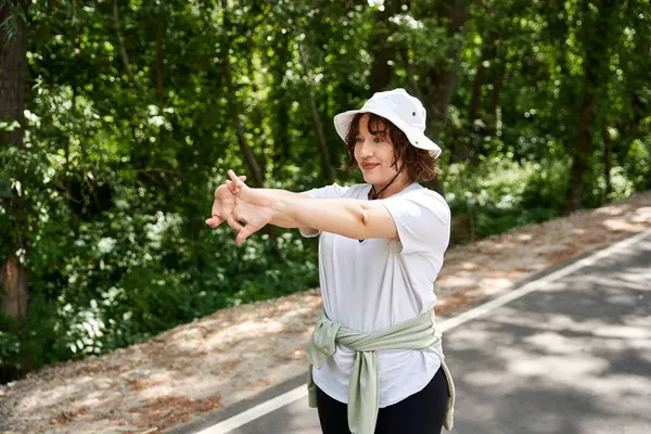 A pretty woman enjoys her outdoor workout, stretching in a lush green environment with joy. — Stock Photo